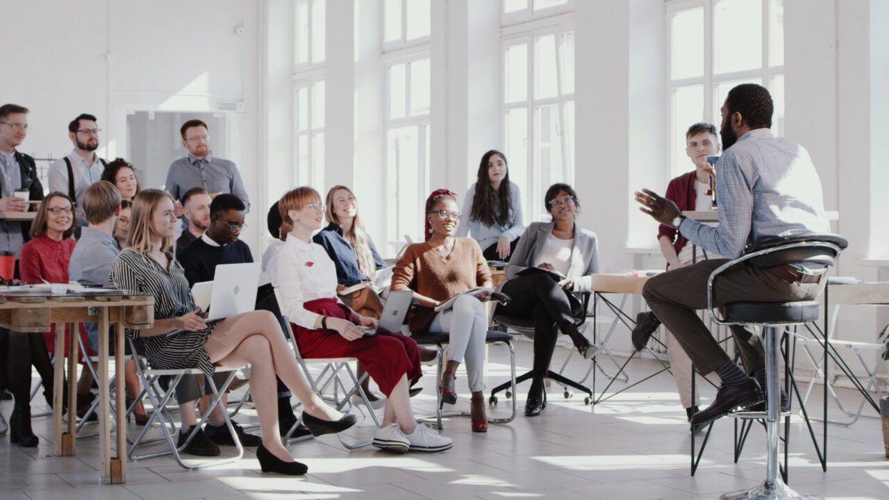 RED EPIC Young happy black CEO businessman giving a speech for multiethnic managers team at trendy office slow motion. Healthy workplace, corporate employees listen to male boss at finance seminar.