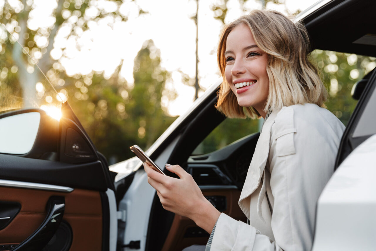 fuhrparkmanagement: Frau sitzt in ihrem Auto mit einem Handy in der Hand