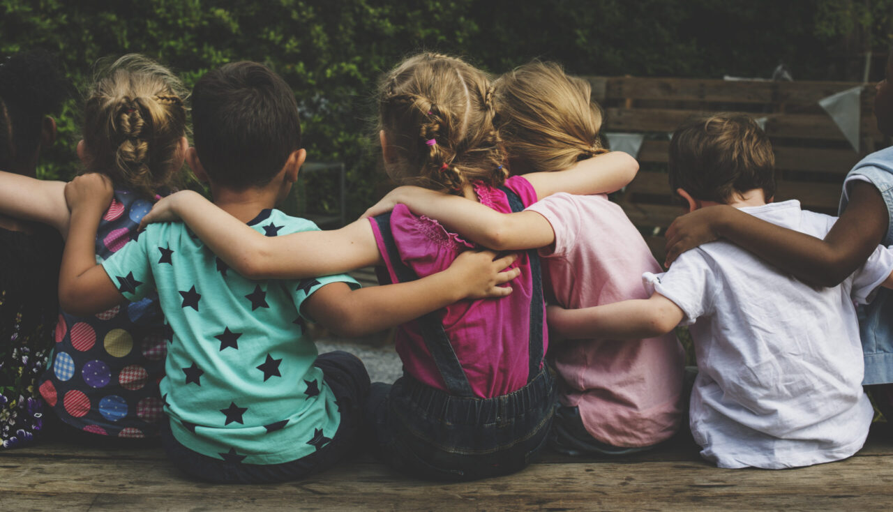 Kitazuschuss: Gruppe von Kindern sitzt Arm in Arm nebeneinander