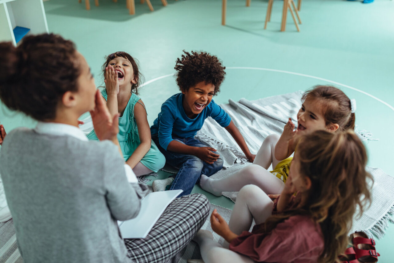 Kitazuschuss: Lachende Kinder spielen mit Lehrerin