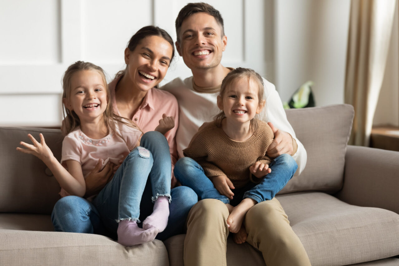 Kitazuschuss: Glückliche Familie sitzt lachend auf der Couch